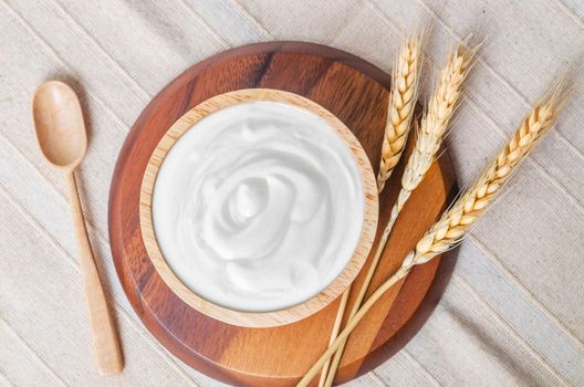 Greek yogurt in a wooden bowl and dry barley on tablecloth.