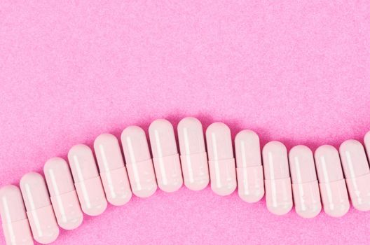 Pink capsule pills on pink background with copy space.