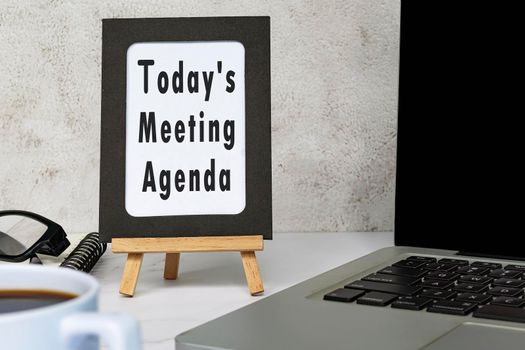 Today's meeting agenda text written on chalkboard with notebook on white desk.