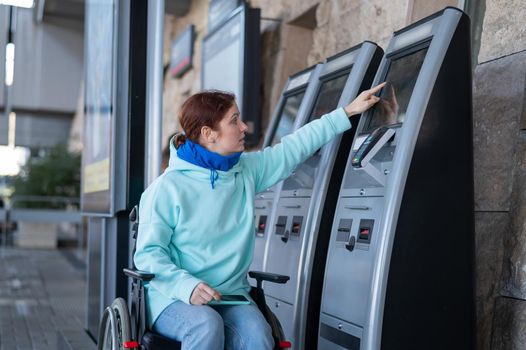 Caucasian woman in a wheelchair buys a train ticket at a self-service checkout.