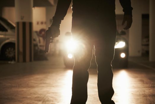 Shadow of fear. A criminal holding a revolver about to hijack someone in an underground parking lot.