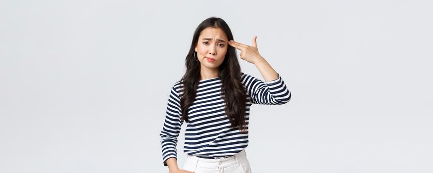 Lifestyle, people emotions and casual concept. Annoyed and pissed-off young woman cant stand this anymore, showing fake gun over head as if shooting herself from annoyance