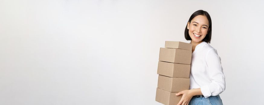 Portrait of young asian woman holding boxes, carry delivery goods. Korean female entrepreneur assemble order, standing voer white background
