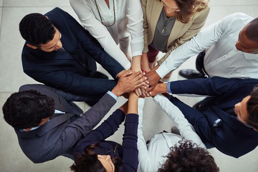 Greatness can only be achieved with the support of all. High angle shot of a group of businesspeople joining their hands together in unity.