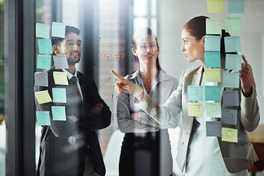 Working out their plan as a team. Shot of a group of businesspeople brainstorming on a glass wall with sticky notes in an office.