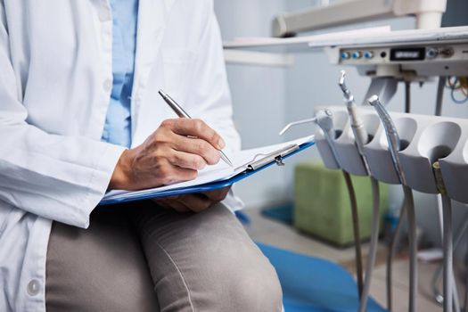 Shot of an unrecognisable dentist writing notes on a piece of paper.