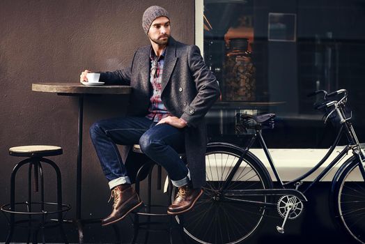 Coffee is always a good idea. Shot of a handsome young man in winter wear having a beverage at a sidewalk cafe.