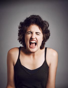 Get me out of here. Studio shot of an attractive young woman screaming with her eyes closed while standing against a grey background.
