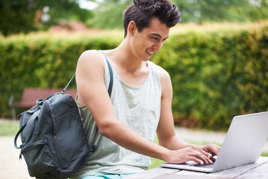 Networking anywhere and anytime. A handsome young man typing on his laptop while sitting in the park.