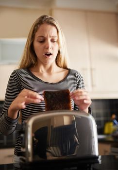Looks like its going to be one of those days. Shot of a young woman removing a slice of burnt toast from a toaster at home.