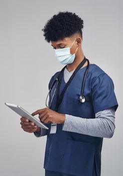 Wear your mask, its good for the numbers. Shot of a male nurse holding a digital tablet while standing against a grey background.