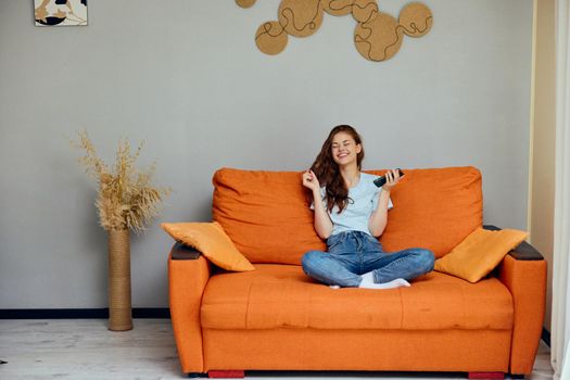 portrait of a woman chatting on the orange couch with a smartphone unaltered