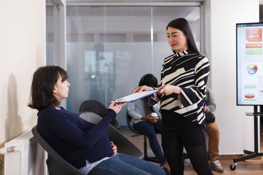 Pregnant candidate giving cv resume to asian manager during job recruiting for human resources job offer. Multi ethnic people waiting in lobby area of startup company office. Concept of hiring process