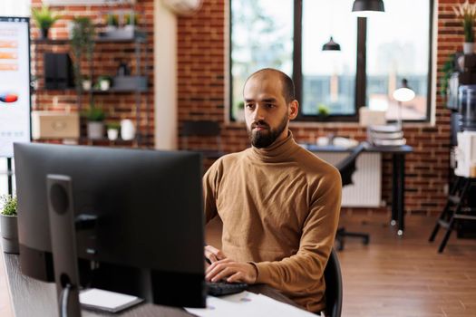 Marketing company employee sitting at desk, developing management plan while using work computer.