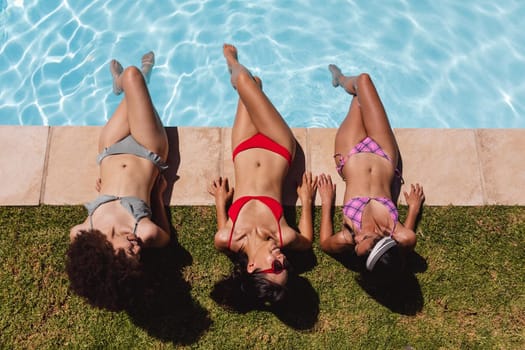 Diverse group of female friends sunbathing by pool and talking. Hanging out and relaxing outdoors in summer.
