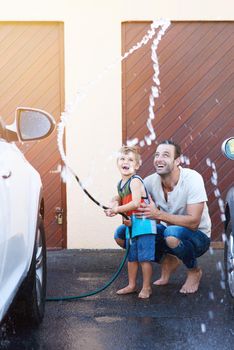 Full length shot of a father and son playing with a hosepipe while washing a car together.
