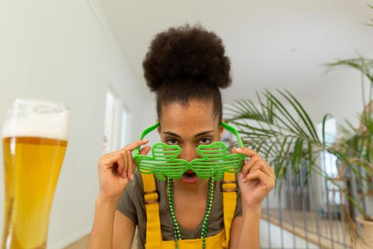 Mixed race woman celebrating st patrick's day making video call looking over shamrock glasses