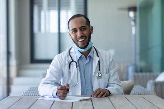 Portrait of mixed race male doctor wearing face mask looking at the camera and smiling