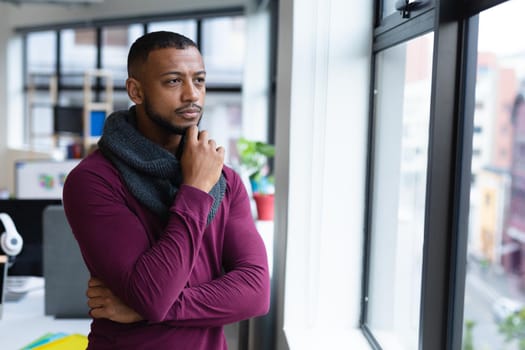 Mixed race businessman in thought looking through window in creative office