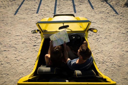 Happy caucasian couple sitting in beach buggy by the sea reading roadmap
