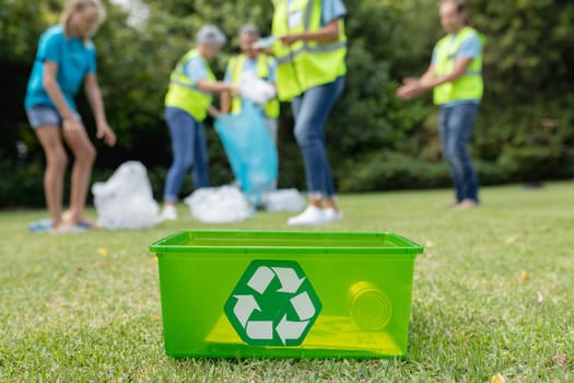 Caucasian group of men and women collecting rubbish in field with recycling box in foreground