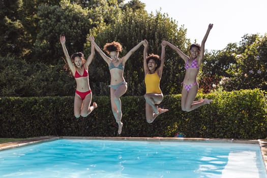 Diverse group of female friends having fun and jumping into water at a pool party. hanging out and relaxing outdoors in summer.