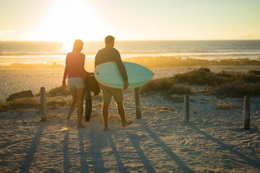 Caucasian couple on the beach carrying surfboard during sunset