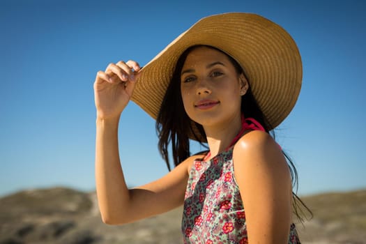 Portrait of caucasian woman by the sea wearing straw hat looking to camera