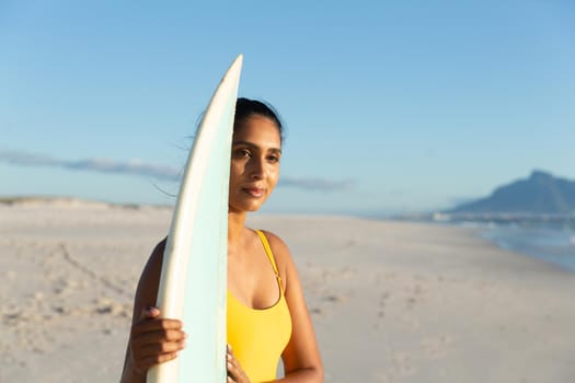Happy mixed race woman carrying surfboard on the beach