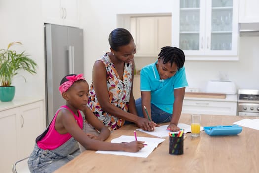 African american mother with daughter and son doing school work in kitchen