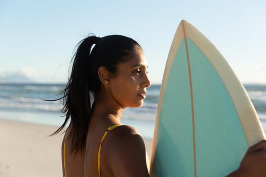 Mixed race woman carrying surfboard on the beach