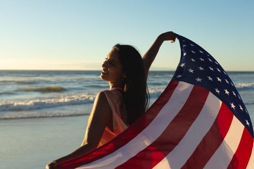 Mixed race patriotic woman on the beach holding american flag