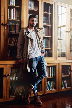 Portrait of a handsome and stylish young man leaning against a bookcase at home.