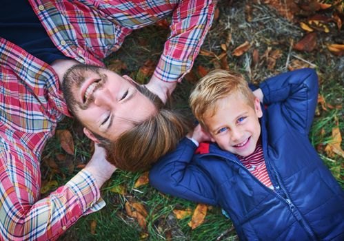 High angle portrait of a handsome young man and his son lying on the grass outside during autumn.