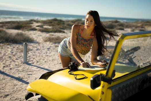 Happy caucasian woman reading roadmap on beach buggy by the sea