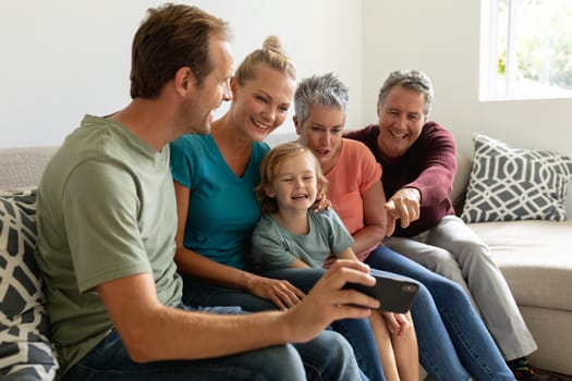 Caucasian father sitting on couch with with his wife, parents and son looking at his smartphone