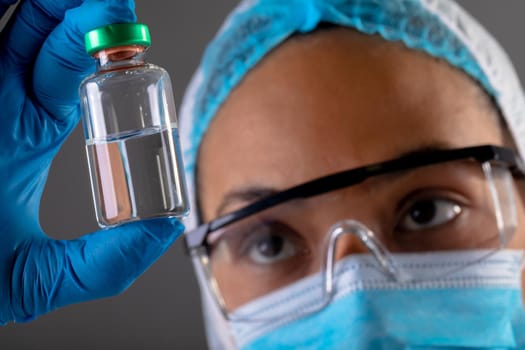 Close up of female surgeon holding covid-19 vaccine bottle against grey background