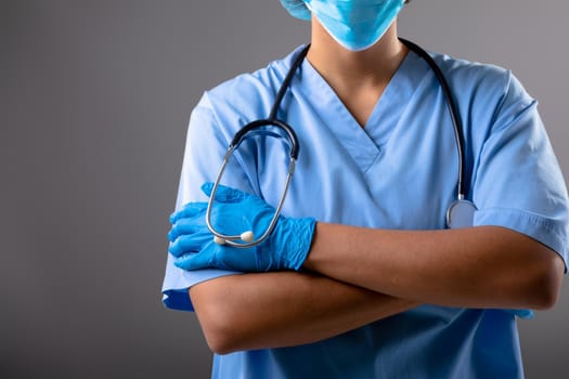 Mid section of female surgeon wearing face mask against grey background