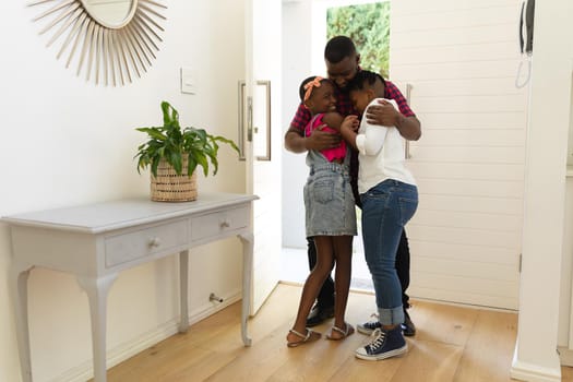 Happy african american father hugging son and daughter in hallway of home. staying at home in isolation during quarantine lockdown.