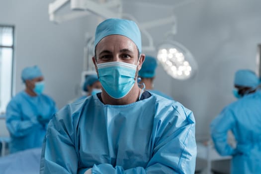 Portrait of caucasian male surgeon wearing face mask and protective clothing in operating theatre