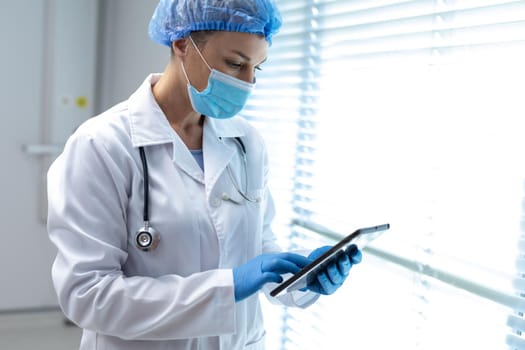 Caucasian female doctor wearing mask and latex gloves using tablet