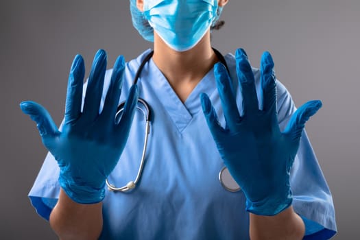 Mid section of female surgeon wearing surgical gloves against grey background