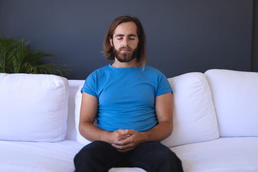 Caucasian man sitting on sofa meditating with eyes closed