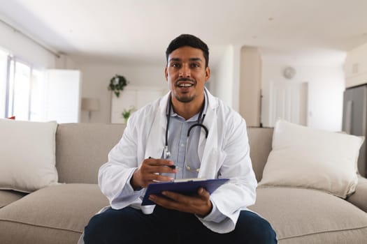 Hispanic male doctor sitting on couch talking during consultation video call