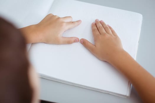Blind caucasian schoolboy sitting at desk reading braille book with fingers