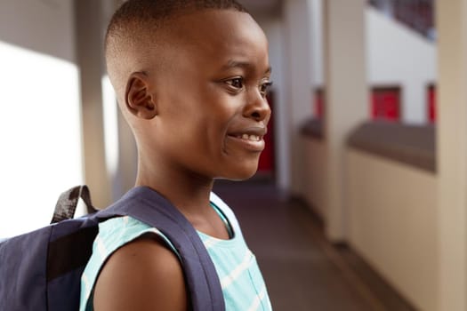 Smiling african american schoolboy wearing schoolbag standing in school corridor