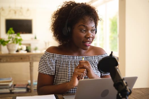 Happy african american woman wearing headphones and using microphone, talking during podcast