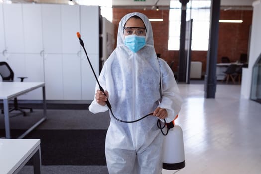 Portrait of cleaner wearing ppe suit, glasses and mask disinfecting office workspace