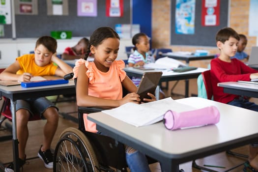 Disabled african american girl using digital tablet while sitting on wheelchair at elementary school