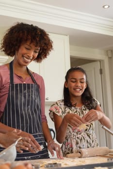 Happy african american mother with daughter baking in kitchen, cutting cookies